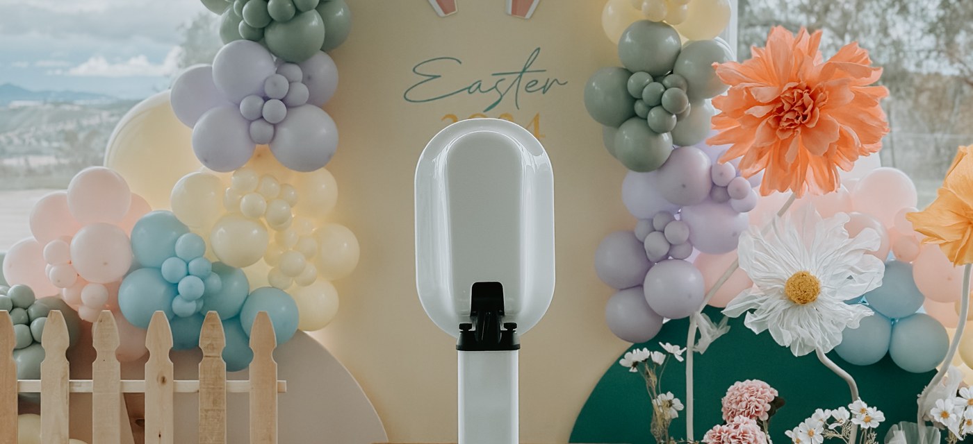 The booth set up beside a pastel balloon arch and paper flowers indoors