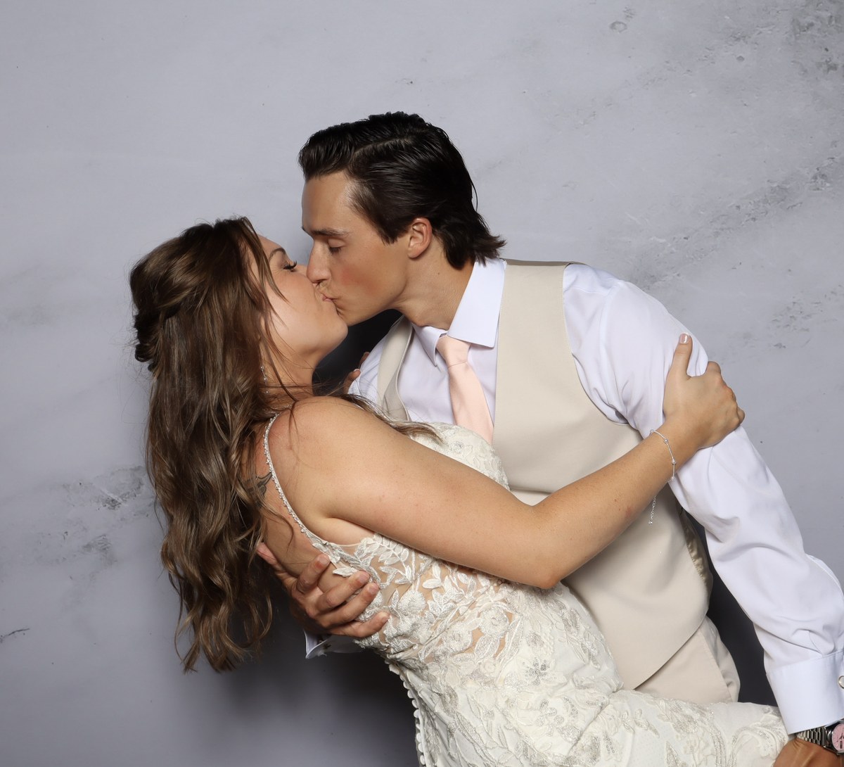 A bride and groom kissing in front of a grey marble backdrop, lit by studio lighting
