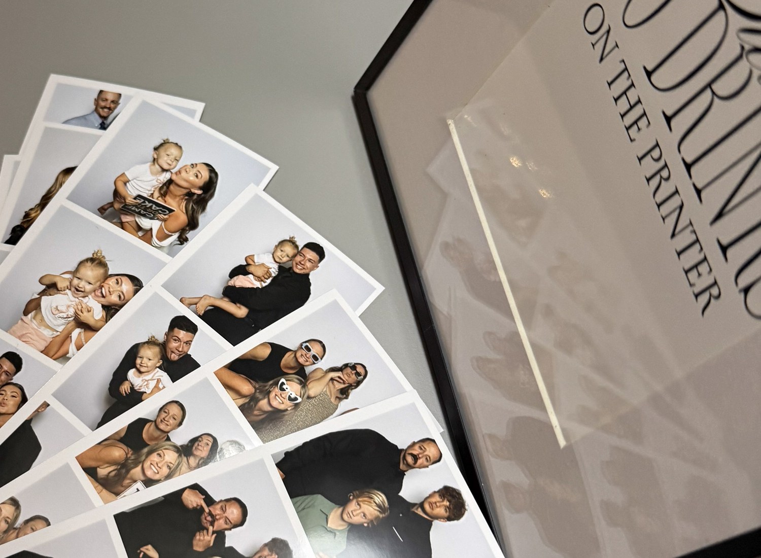 Freshly printed photo strips fanned out on a table beside a framed sign