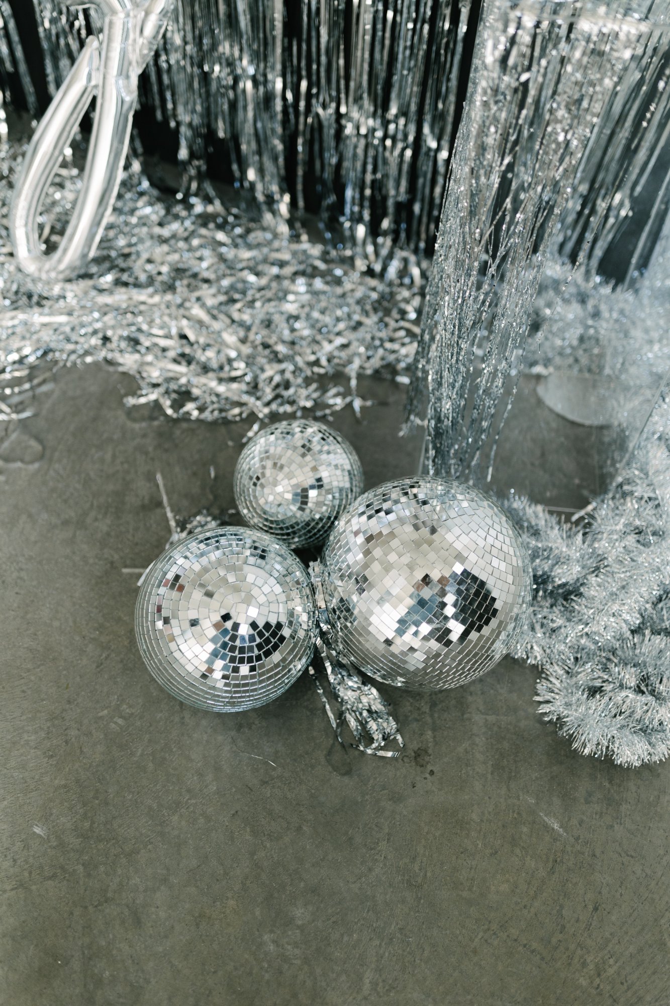 Three mirrored disco balls on the floor among silver tinsel and a foil fringe curtain