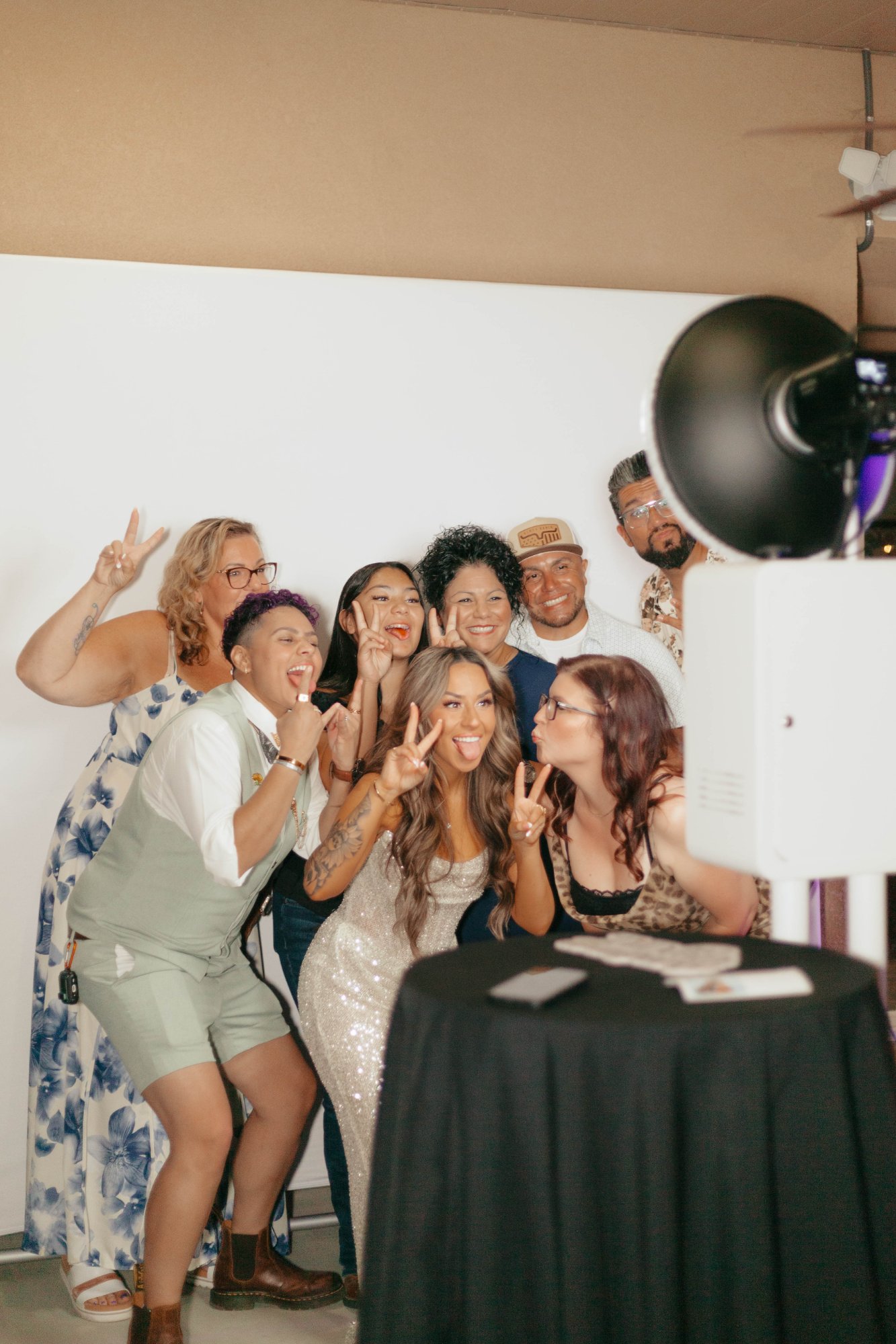 Guests at a photo booth with a studio light and white backdrop, several of them flashing peace signs
